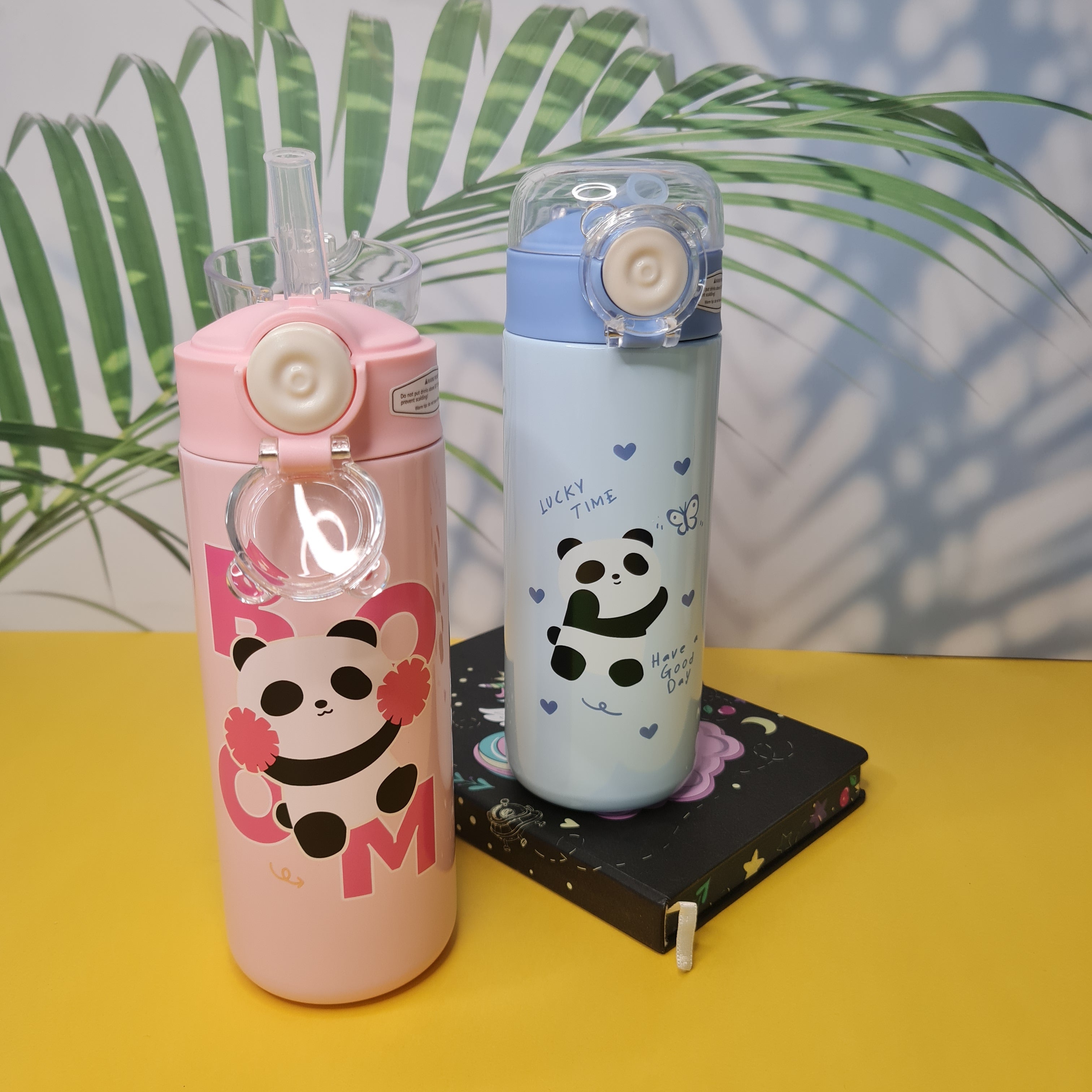 Two panda-themed water bottles on a yellow surface with a leafy background
